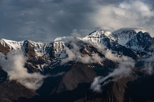 Dramatic landscape of snow-covered mountains with clouds under a winter sky.