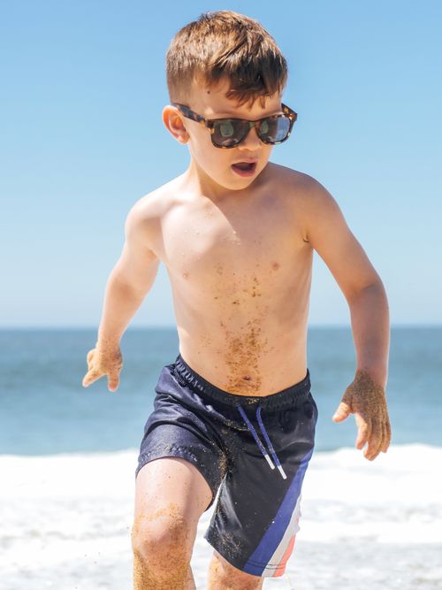 Free Boy enjoying a playful day on a sunny beach, capturing a carefree summer moment. Stock Photo