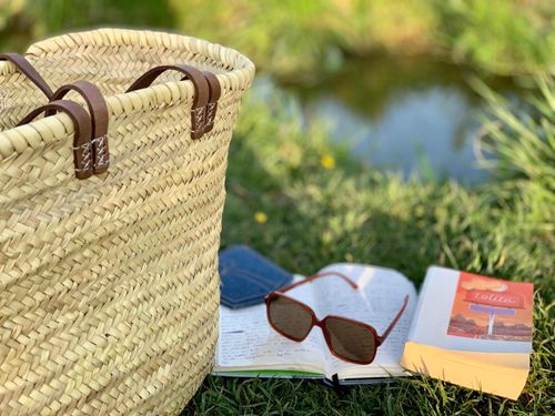 Free A relaxing outdoor setting featuring a woven bag, sunglasses, and an open book on grass. Stock Photo
