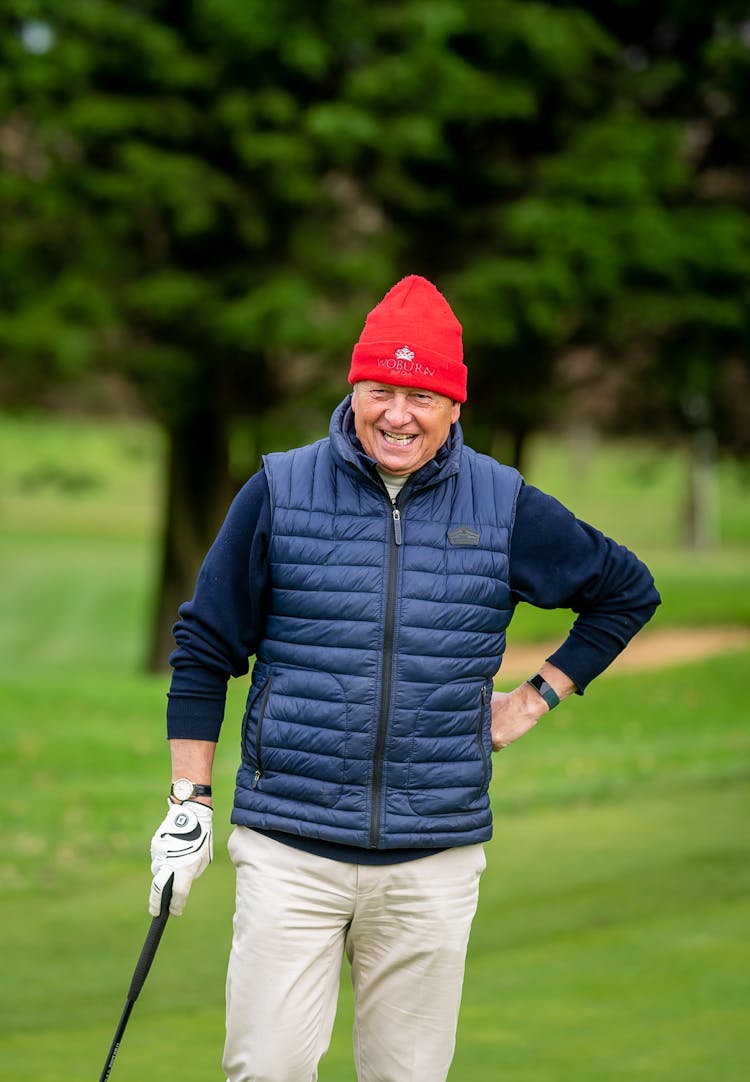 A Man In Blue Vest And Red Beanie Holding A Golf Club