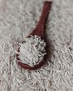 From above of raw white rice grains on wooden spoon placed on pile