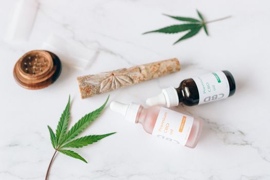 Flat lay of CBD oil dropper bottles and hemp leaves on a marble surface.