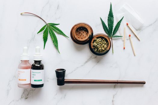 Top view of cannabis products including CBD oils, leaves, and smoking accessories on a marble surface.