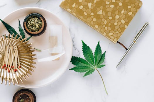 Aesthetic flat lay of cannabis-related items including a cannabis leaf, matches, and a notebook on a marble surface.
