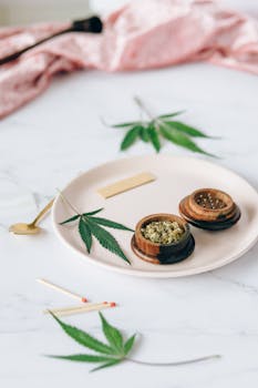 Aesthetic display of marijuana leaves and wooden grinder on white plate with matches.