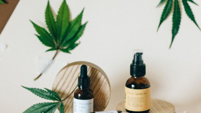 Assortment of CBD oil bottles and capsules with cannabis leaves on a neutral surface