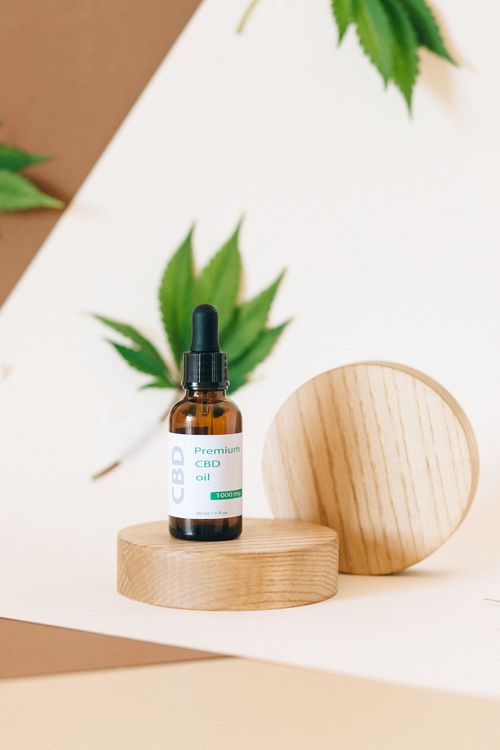 Free A bottle of premium CBD oil on a wooden stand with cannabis leaves in the background. Stock Photo