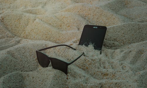 Free Photo of Phone and Sunglasses on Sand Stock Photo