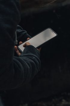 Crop anonymous person in casual clothes standing and using smartphone against dark background