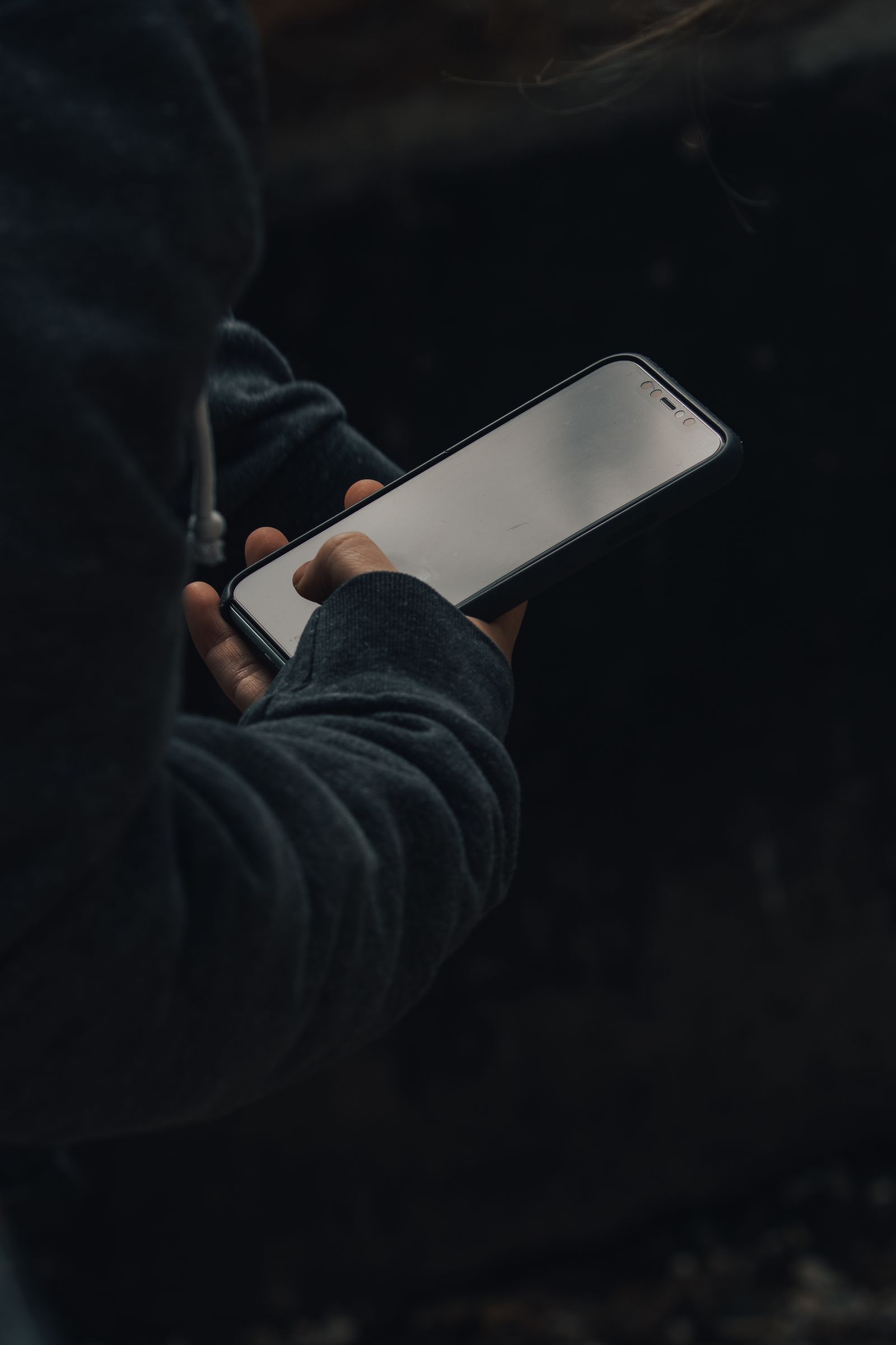 An anonymous person browsing a smartphone at night against a dark background