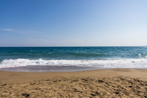 Free Serene sandy beach with gentle ocean waves under a clear blue sky, perfect for relaxation. Stock Photo