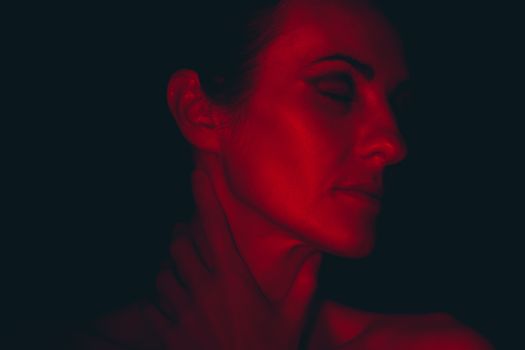 Close-up portrait of a woman with eyes closed, illuminated by red light, creating a moody and artistic atmosphere.