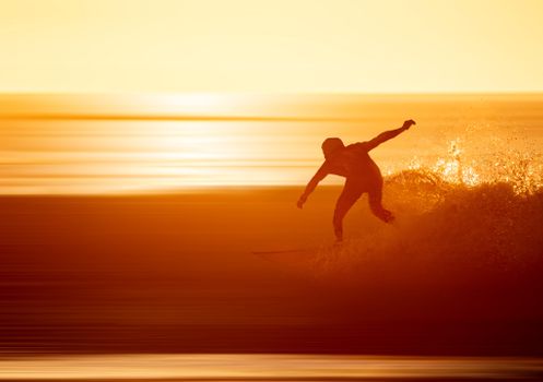 A surfer skillfully maneuvers a wave against the dramatic backdrop of a golden sunset.