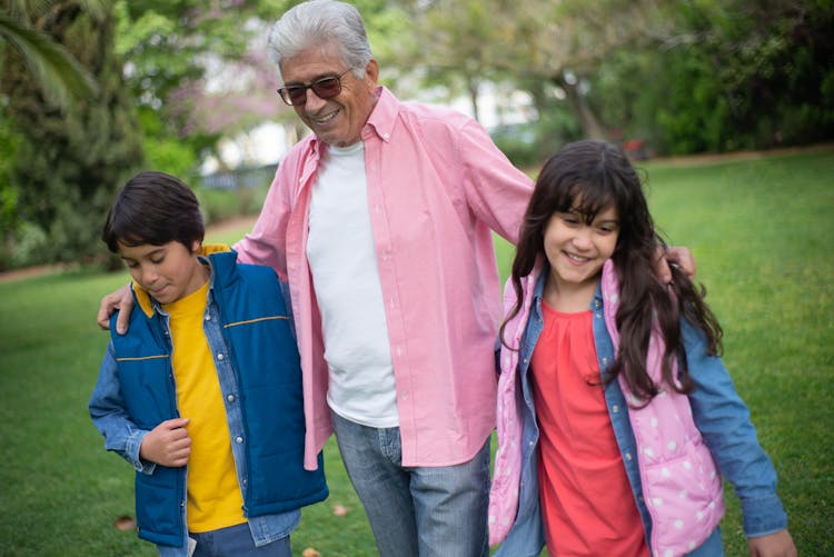 An Elderly Man Walking With His Grandchildren At A Park