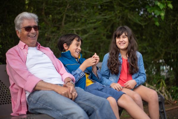 A grandfather laughing with two grandchildren on a park bench.
