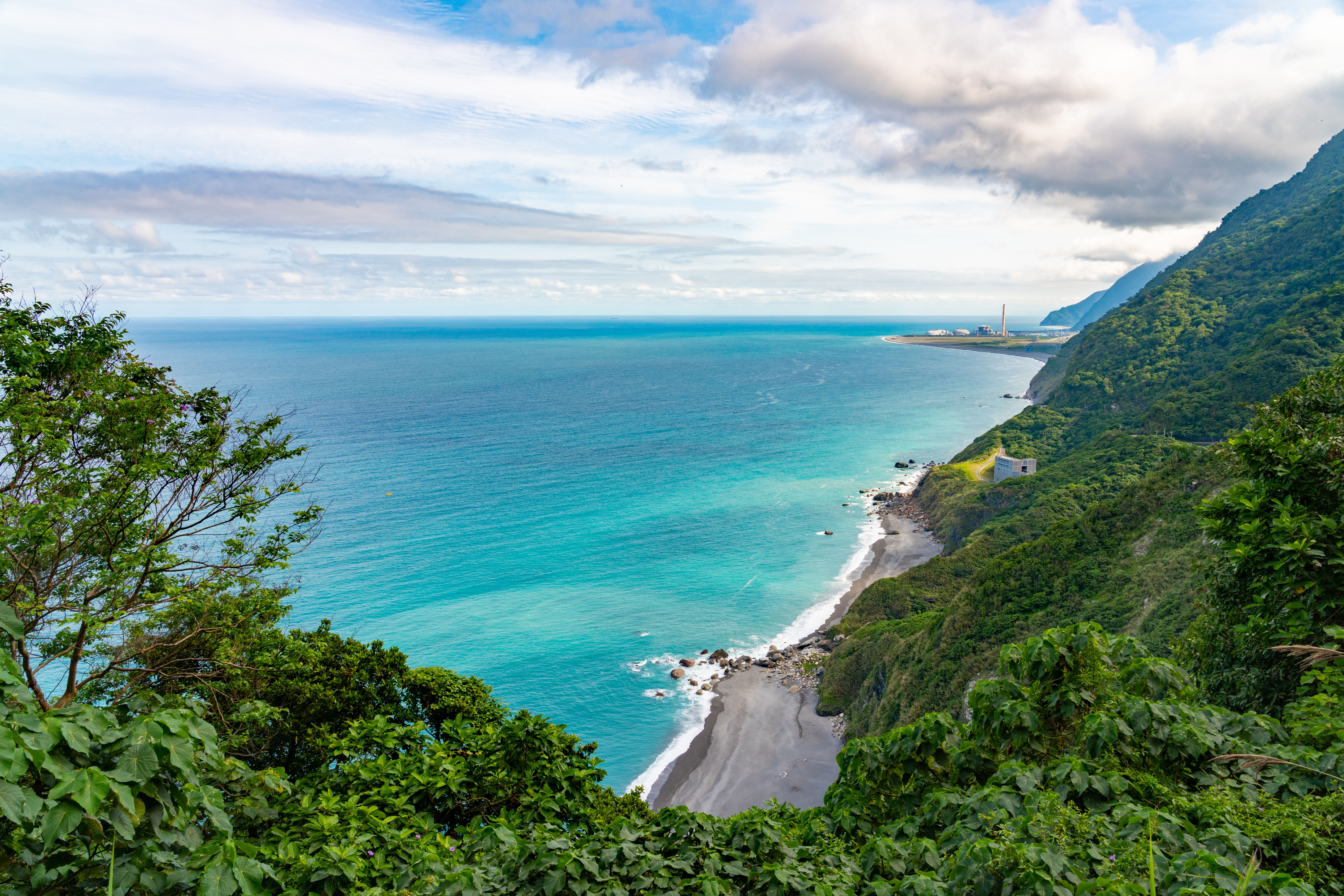 Breathtaking view of Taiwan's coastline with lush green cliffs and turquoise sea under a partly cloudy sky.