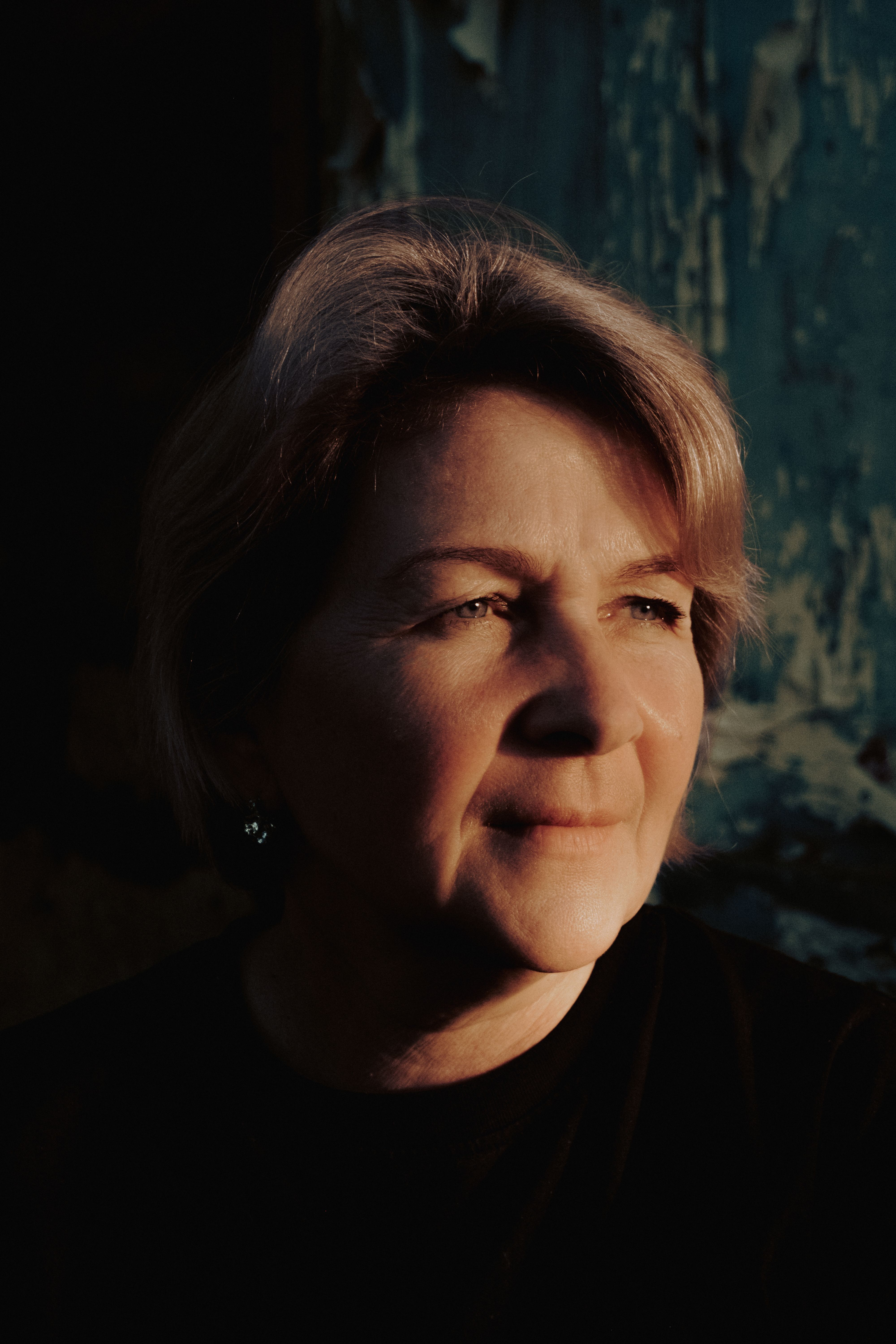 Senior female with short fair hair looking away thoughtfully against shabby green surface
