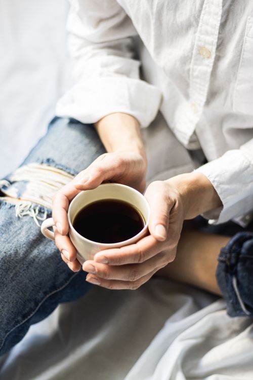 Free Person holding a cup of black coffee while sitting in casual attire, offering a relaxed ambiance. Stock Photo