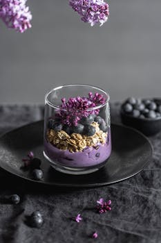 A stylish vertical shot of a blueberry granola parfait with lilac flowers.