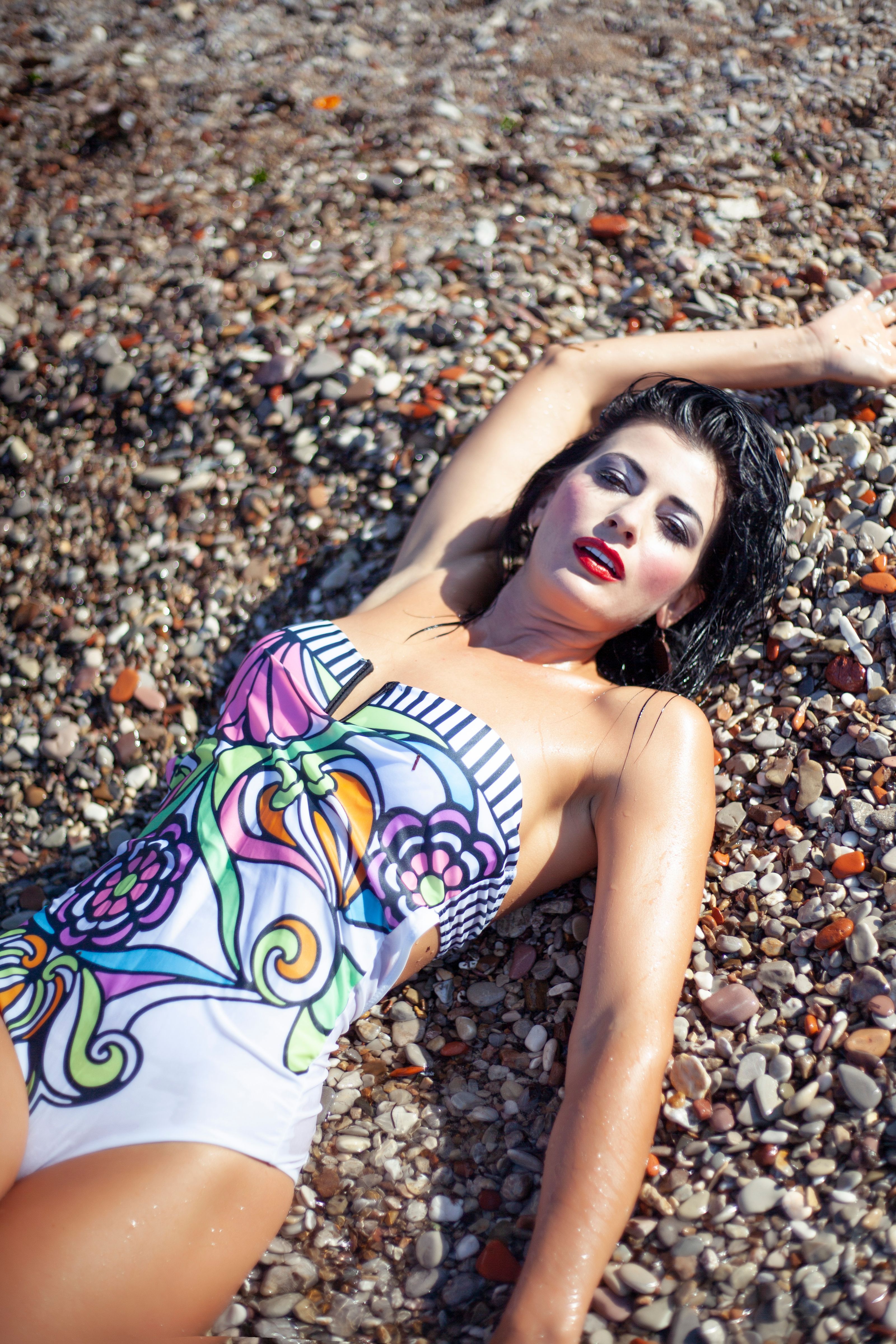 Mulher fashion em um maiô colorido deitada em uma praia de pedras, aproveitando o sol de verão.