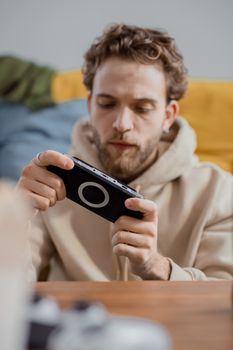 A young man intensely focused on gaming with a handheld console while seated indoors.