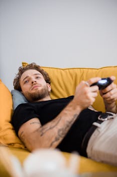 Young man lying on couch playing video games, focused on screen.
