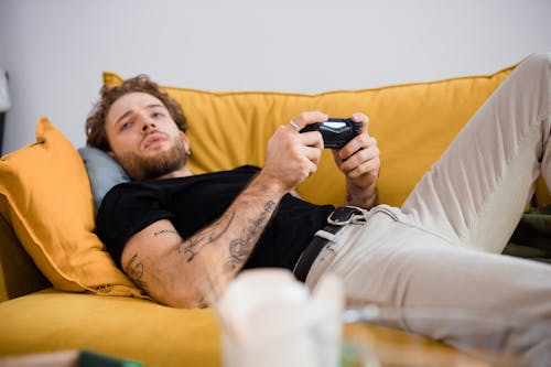 Free Man in Black T-shirt and Beige Pants Lying on Couch Holding a Remote Controller Stock Photo