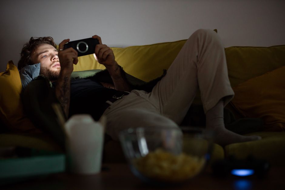 Photo by Ron Lach on Pexels A young man lounges on a sofa while playing games on a handheld device, immersed in the screen's glow. - Photo by Ron Lach on Pexels