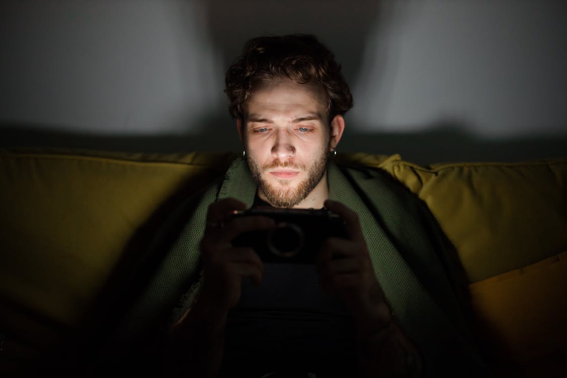 Free Focused young man looking at a smartphone screen, creating a moody atmosphere indoors. Stock Photo