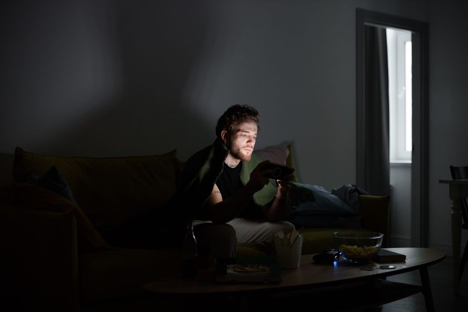 A young man intensely focused on gaming on his smartphone in a dark, cozy room.