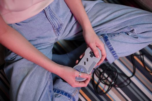 Close-up of a young woman holding a retro game controller indoors, enjoying gaming.