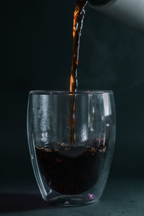 Free Dark aromatic coffee pouring into transparent glass placed on gray surface at daylight Stock Photo