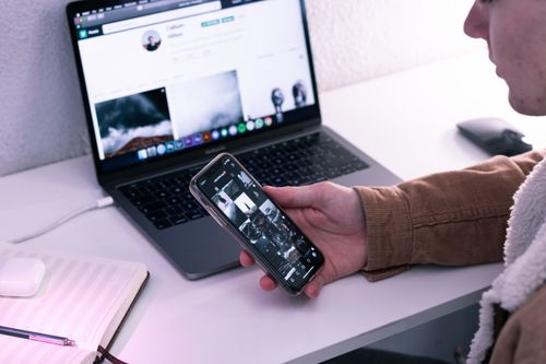 Free High angle of crop male watching photos on mobile phone at table with netbook and opened planner Stock Photo