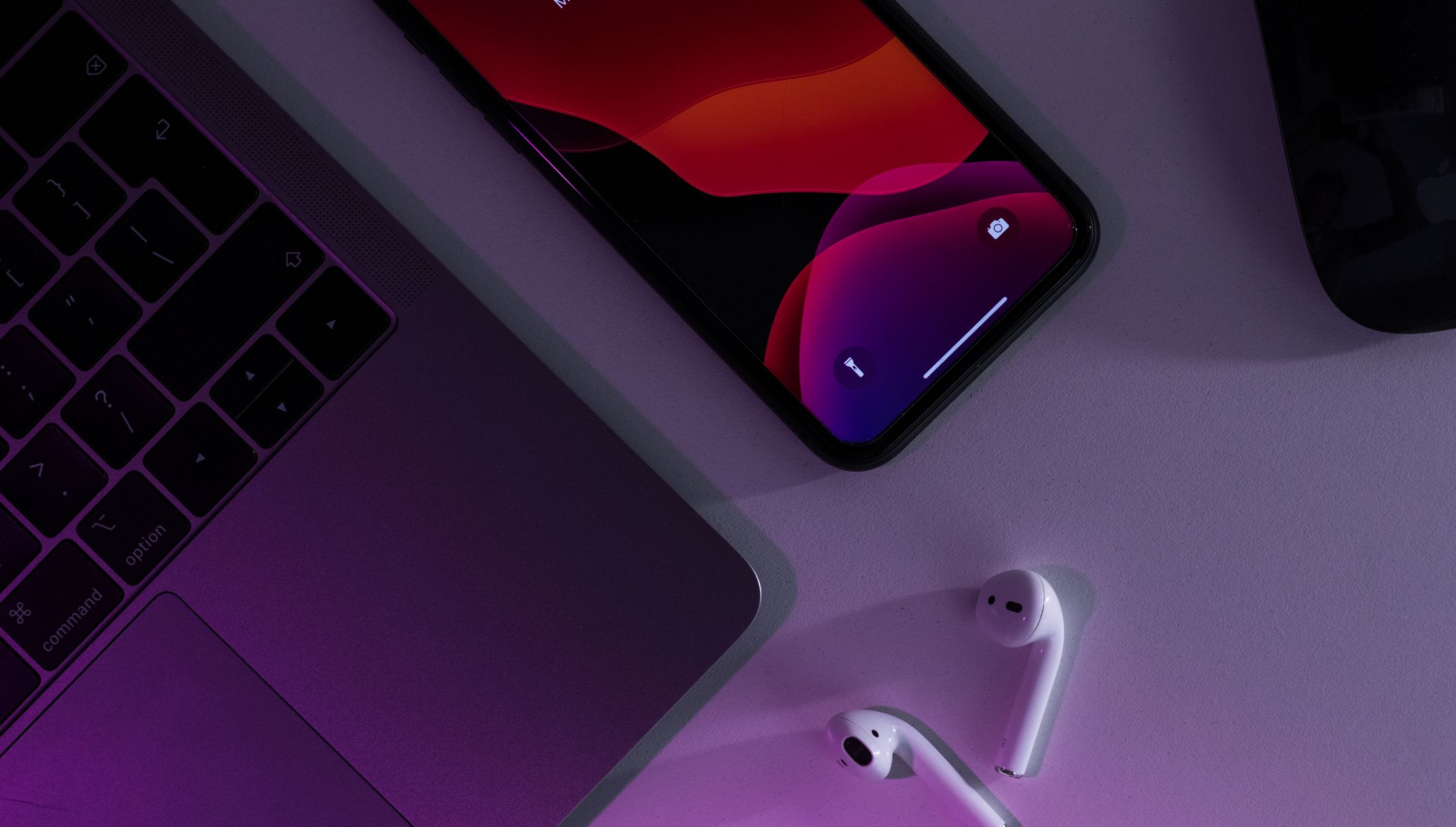 A laptop, smartphone and wireless earbuds on a desk for the weekend flash sale