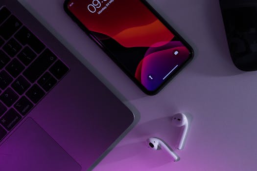 Overhead of cellphone placed near netbook and wireless earbuds on table at convenient workplace