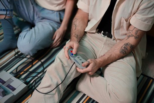 Two adults playing retro video games indoors, focusing on hands holding a controller.