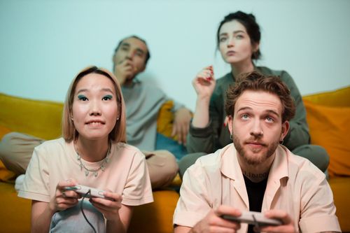 Free Four friends sitting indoors enjoying a gaming session together. Diverse and fun atmosphere. Stock Photo