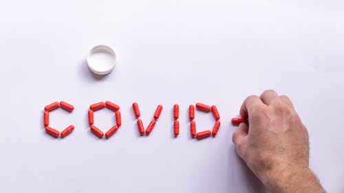 Top view of male making COVID composition with bright capsules for medical treatment on white background