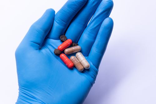 Free Top view of crop anonymous medic in latex glove demonstrating handful of medicines for therapy against white background Stock Photo