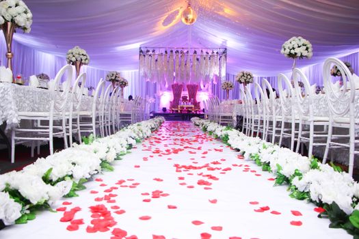 A beautifully decorated wedding hall with white chairs and floral arrangements, creating an elegant atmosphere.