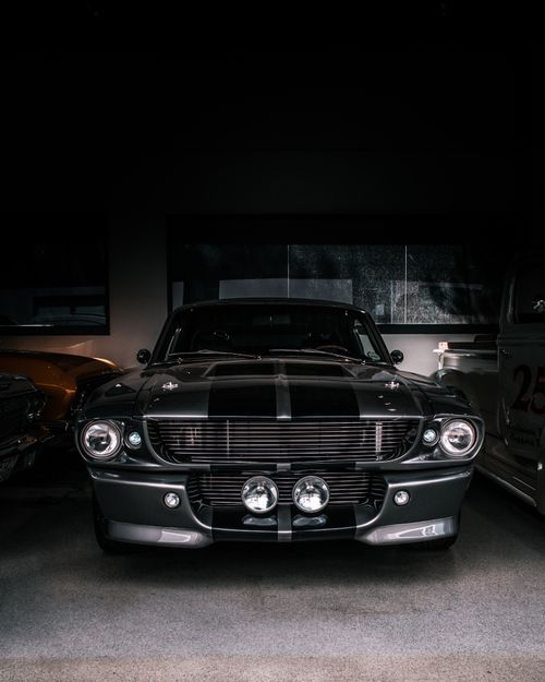 Free Front view of a classic sports car parked in a dimly lit garage, showcasing its elegant design. Stock Photo