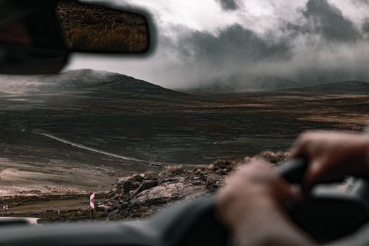 A captivating view from a car driving through misty hills, with dramatic clouds above.