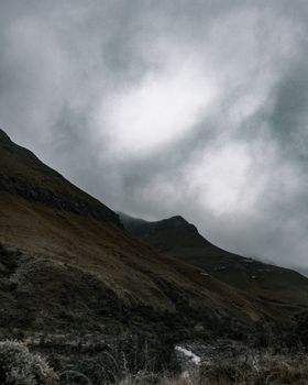 A dramatic mountain landscape with dense clouds creating a haunting and moody atmosphere at dusk.
