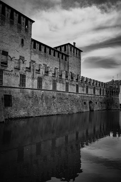 Free Black and white of exterior of aged stone abandoned building reflected on canal surface under cloudy sky Stock Photo