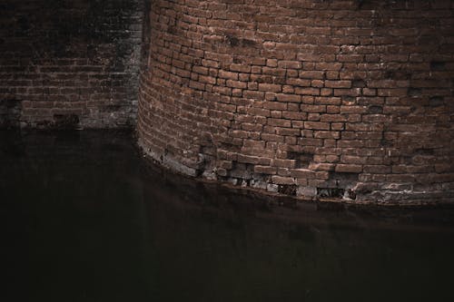 Exterior of aged stone shabby brick walls of abandoned building reflected on calm water surface in gloomy day