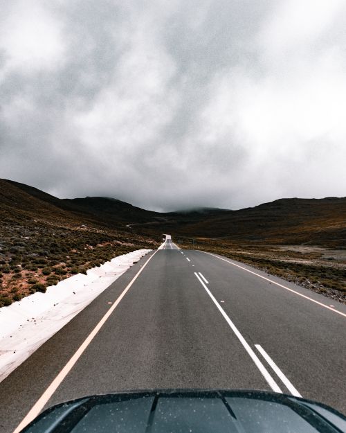 Free Desolate country road stretches beneath heavy clouds, creating a mood of solitude and adventure. Stock Photo