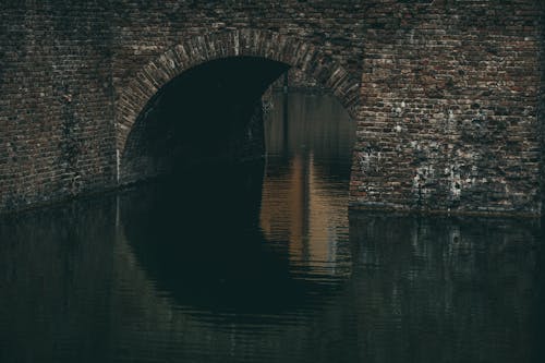 Aged stone brick bridge over calm rippling canal reflected on water surface in gloomy day