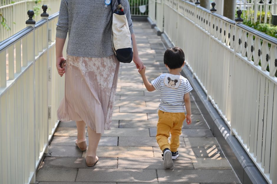 母親と息子が手をつないで、日差しの中の石畳の道を歩いています。