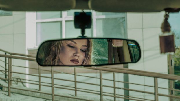Reflection of attractive lady in rearview mirror of car parked in front of building
