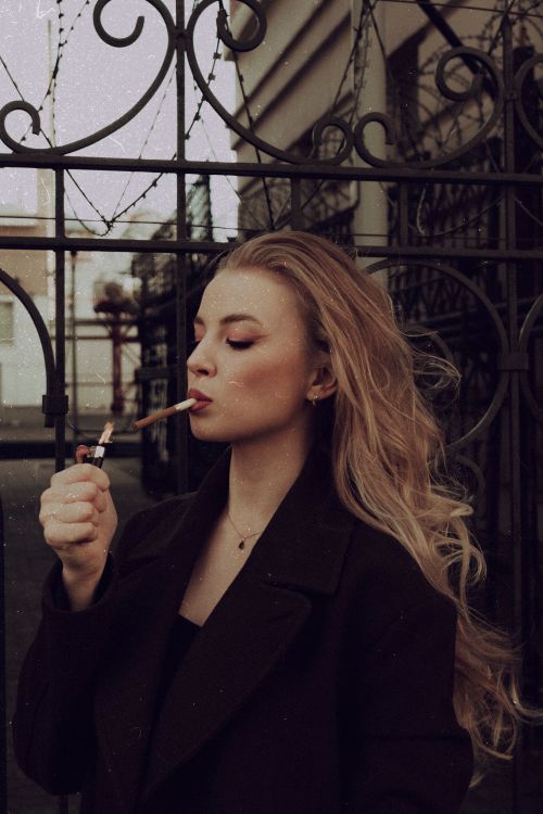 Free Elegant young woman lighting a cigarette outdoors, exuding a sophisticated and moody vibe. Stock Photo